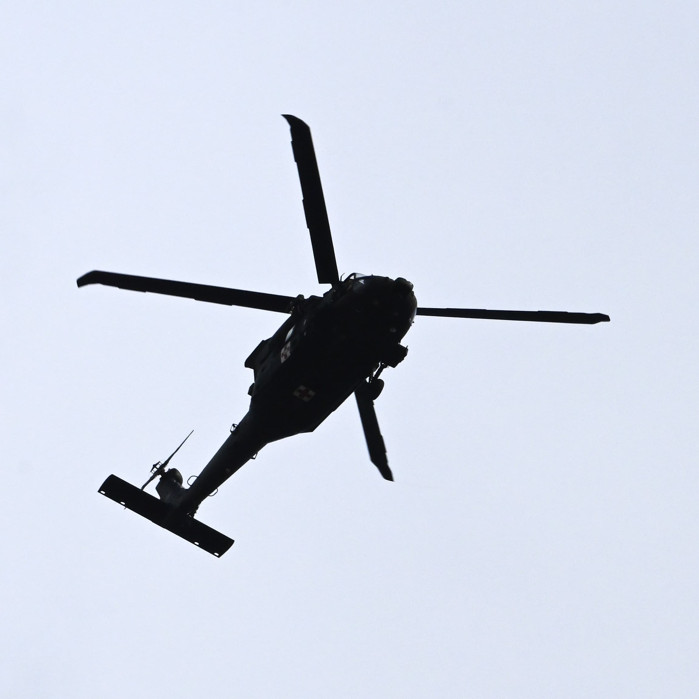 A helicopter in flight, silhouetted from below against a pale overcast sky.