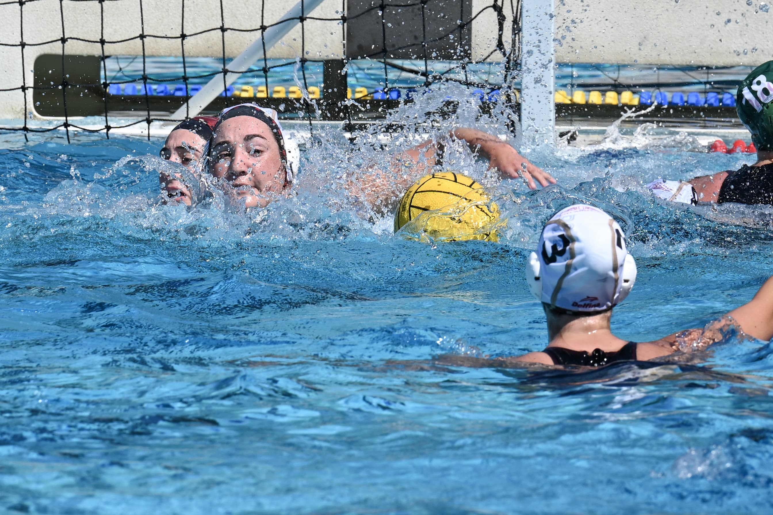 A water polo goalkeeper defending the net as the ball flies toward the goal.