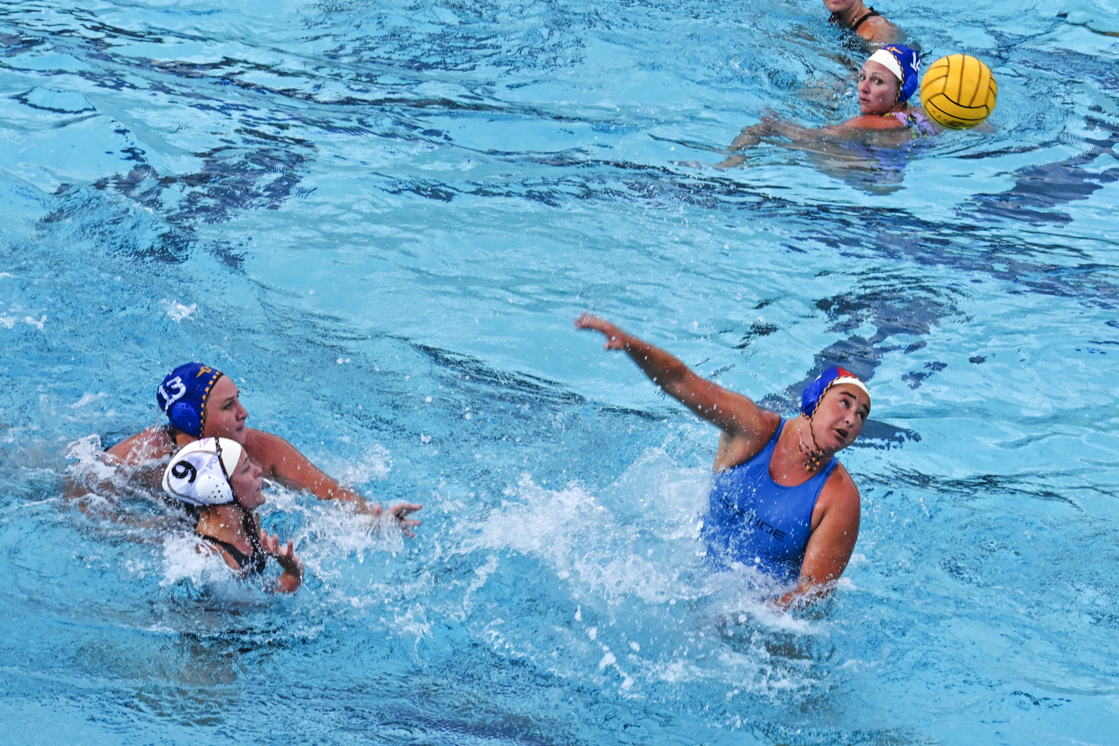 Water polo players in open water mid-play, one reaching for a pass as teammates look on.