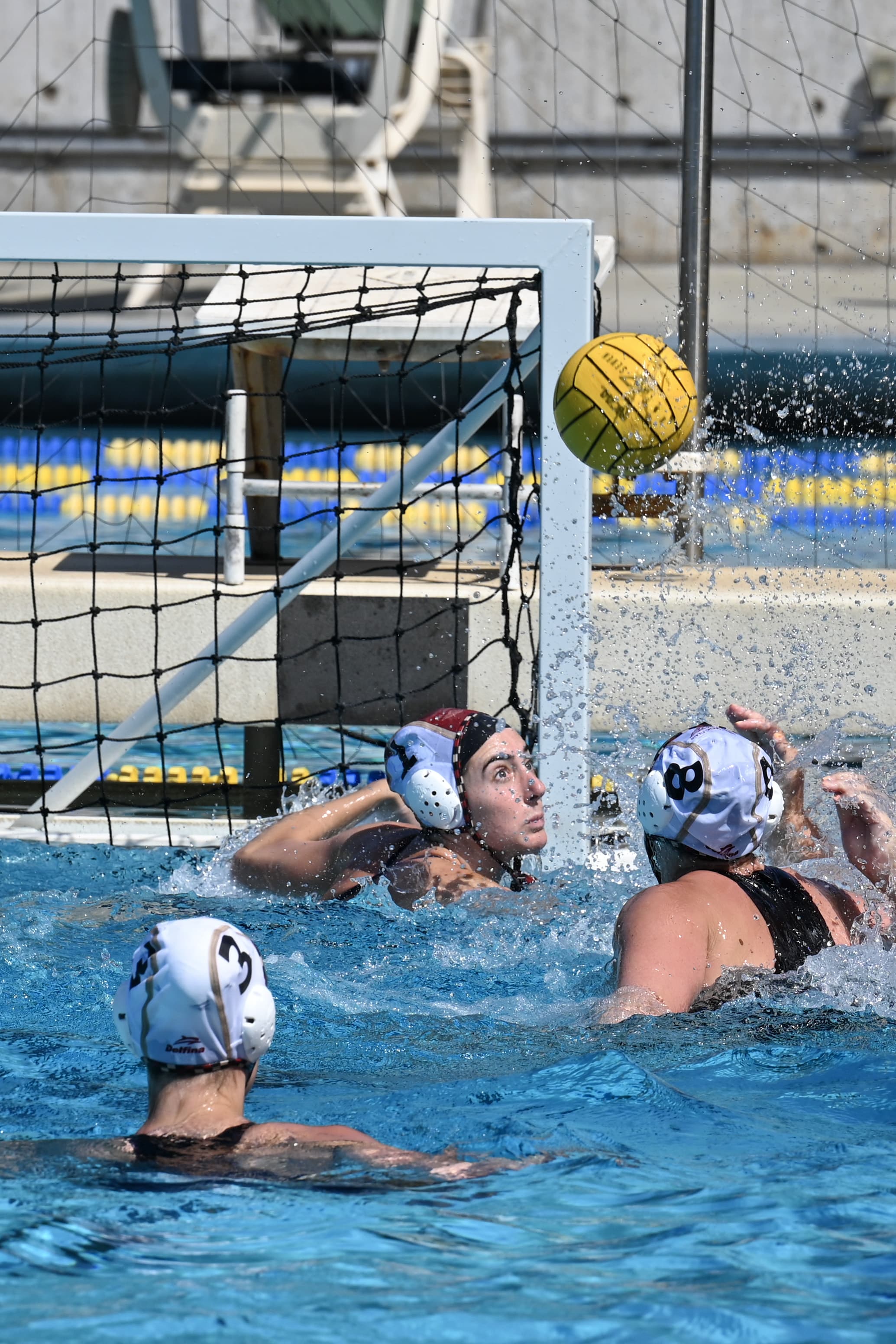 A water polo player mid-throw, arm raised overhead with the ball, defenders closing in.